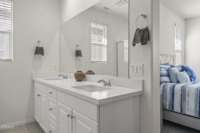 ensuite bathroom with double vanity, baseboards, visible vents, and a sink