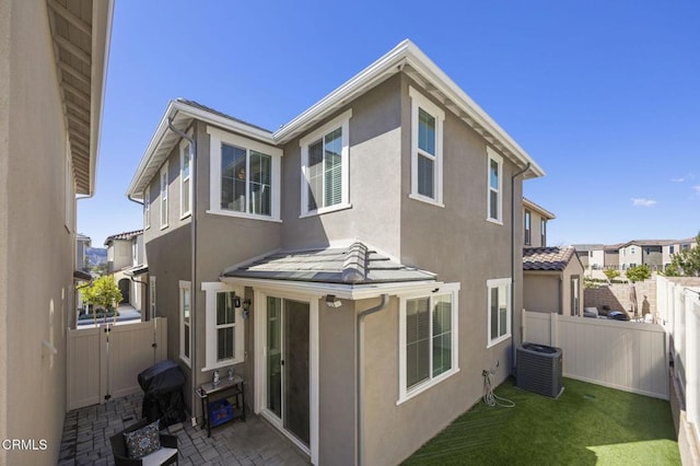 back of property with a tiled roof, a fenced backyard, stucco siding, and central AC unit
