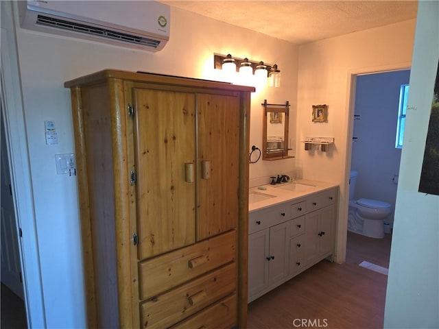 bathroom with toilet, double vanity, wood finished floors, a wall mounted AC, and a sink