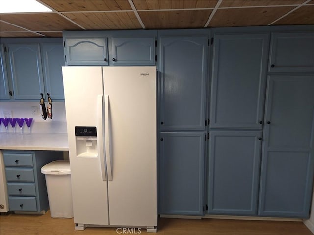 kitchen with light countertops, white refrigerator with ice dispenser, blue cabinets, and light wood finished floors