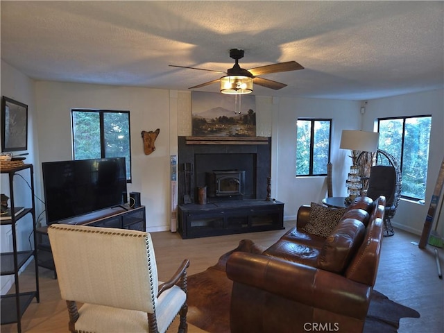 living area featuring baseboards, a ceiling fan, light wood-type flooring, and a textured ceiling