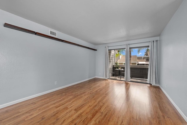 spare room featuring a barn door, wood finished floors, visible vents, and baseboards