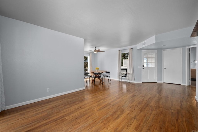 unfurnished living room with visible vents, plenty of natural light, baseboards, and wood finished floors