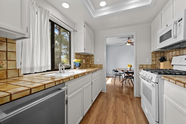 kitchen featuring tile counters, white appliances, white cabinetry, a raised ceiling, and a sink