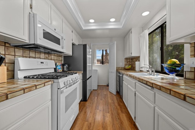 kitchen with ornamental molding, white cabinetry, tile countertops, white appliances, and a raised ceiling