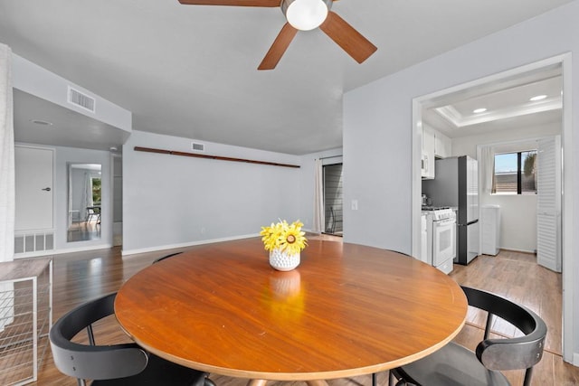 dining space featuring visible vents, light wood-type flooring, and a tray ceiling