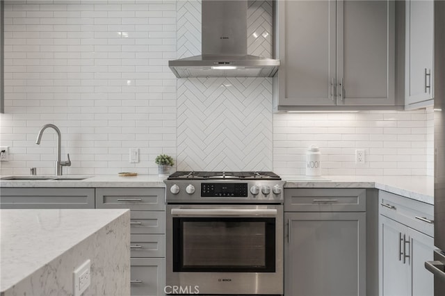 kitchen with gray cabinets, backsplash, gas stove, a sink, and island range hood