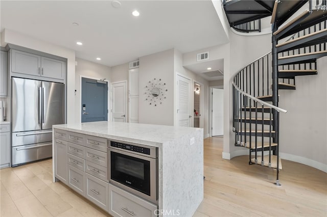 kitchen featuring visible vents, appliances with stainless steel finishes, light stone countertops, gray cabinets, and light wood-type flooring