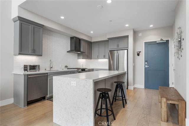 kitchen with stainless steel appliances, a sink, a center island, wall chimney exhaust hood, and a kitchen bar