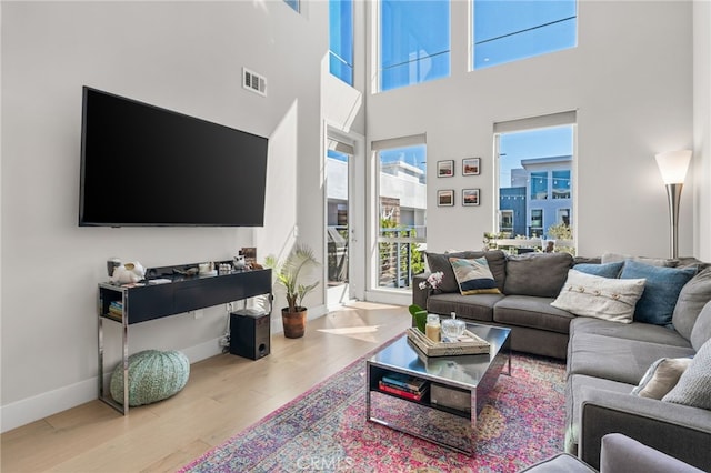 living area featuring visible vents, a towering ceiling, baseboards, and wood finished floors