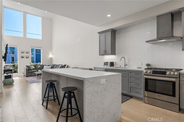 kitchen with stainless steel gas range oven, a sink, gray cabinets, wall chimney exhaust hood, and a kitchen bar