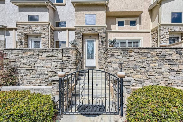 entrance to property with stone siding, a gate, and stucco siding