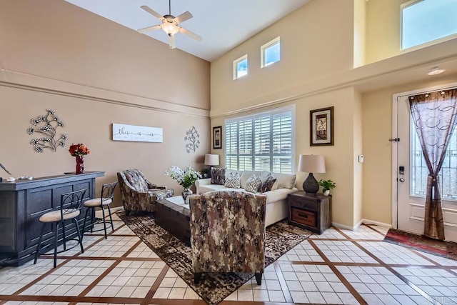 living area with ceiling fan, a high ceiling, light tile patterned flooring, and baseboards