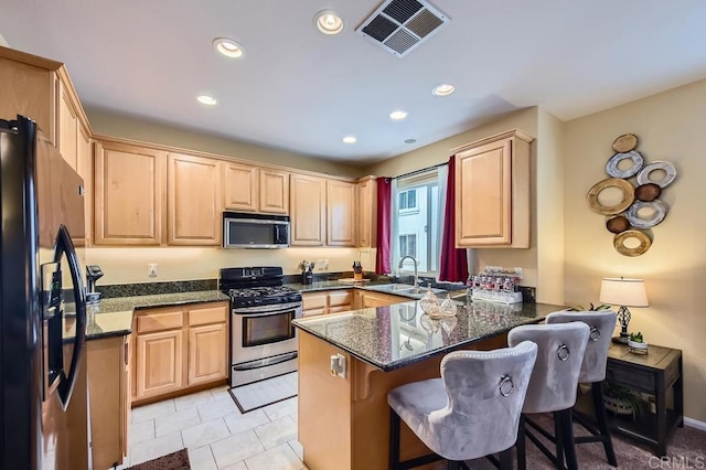 kitchen featuring a peninsula, light brown cabinets, visible vents, and stainless steel appliances