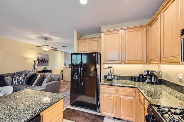 kitchen featuring black refrigerator with ice dispenser, light brown cabinetry, open floor plan, dark stone countertops, and gas range