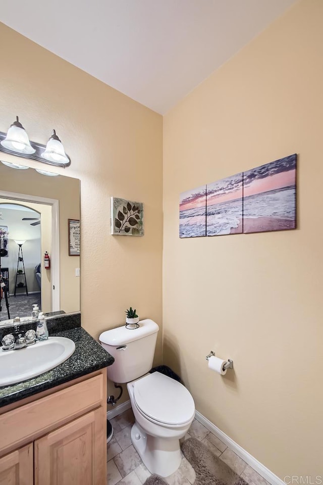 half bath featuring baseboards, vanity, and toilet