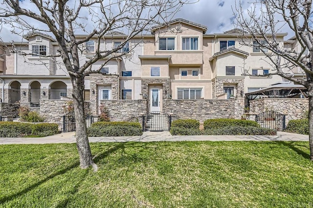 view of front of house with a fenced front yard, stone siding, a front lawn, and stucco siding