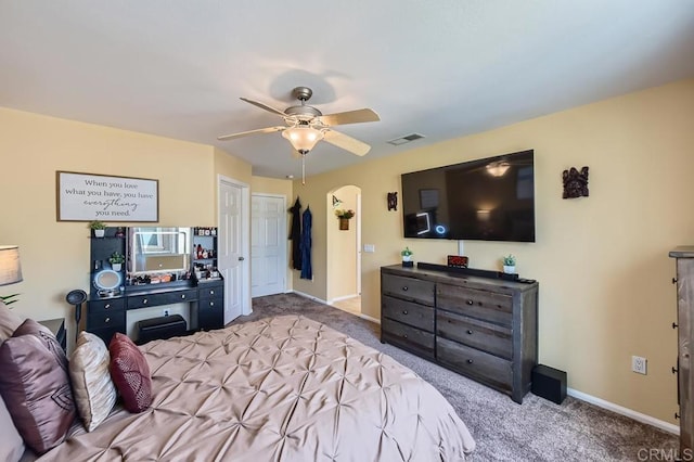 carpeted bedroom with a ceiling fan, arched walkways, visible vents, and baseboards