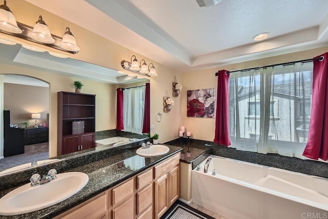 full bathroom featuring double vanity, a tray ceiling, a sink, and a bath