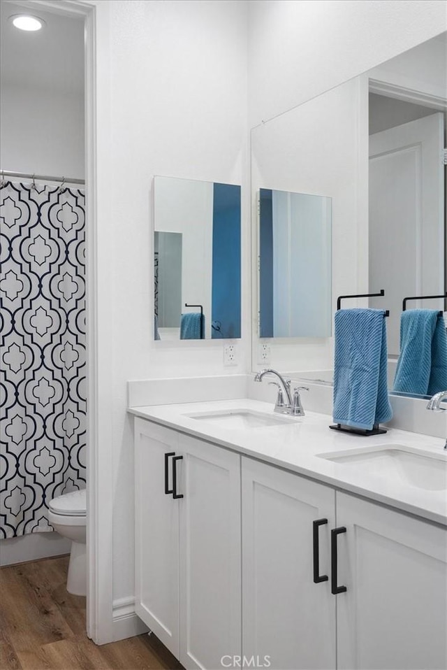 full bath with double vanity, wood finished floors, a sink, and toilet