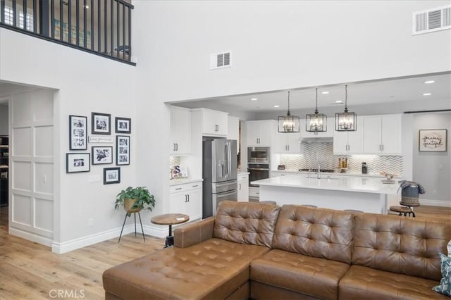 living area featuring baseboards, visible vents, light wood-style flooring, and a high ceiling