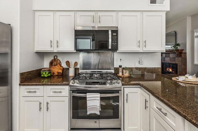 kitchen with tasteful backsplash, a tile fireplace, dark stone countertops, stainless steel appliances, and white cabinetry