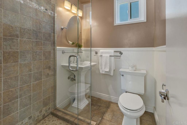 bathroom featuring a wainscoted wall, a tile shower, toilet, and tile patterned floors