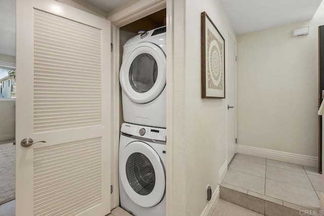 laundry room featuring laundry area, baseboards, stacked washer / drying machine, and tile patterned floors