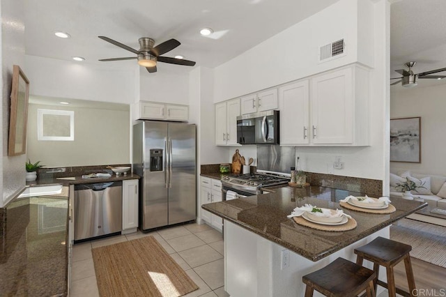 kitchen featuring ceiling fan, stainless steel appliances, visible vents, white cabinetry, and dark stone countertops