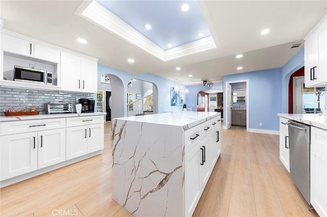 kitchen featuring tasteful backsplash, appliances with stainless steel finishes, a tray ceiling, and light wood-style flooring