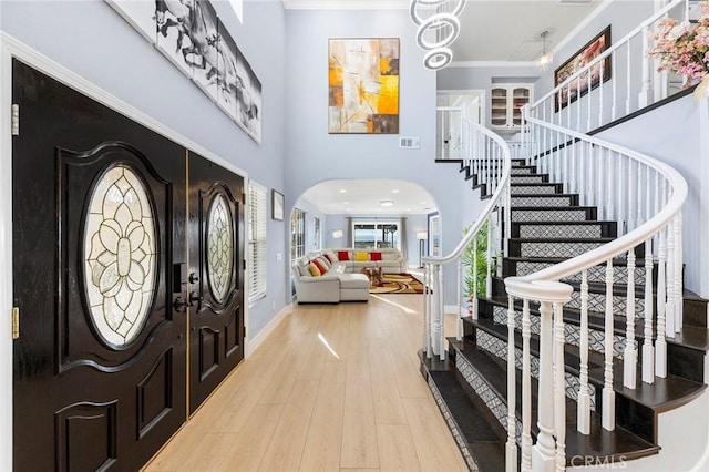 foyer featuring arched walkways, visible vents, light wood-style flooring, stairway, and a high ceiling