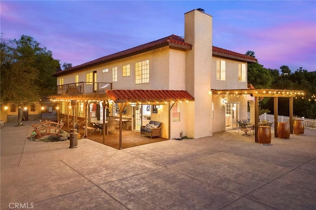 back of house at dusk featuring stucco siding, a patio area, a chimney, and outdoor dining space