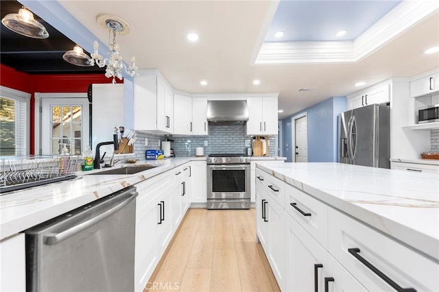 kitchen with stainless steel appliances, a sink, wall chimney range hood, light wood-type flooring, and light stone countertops