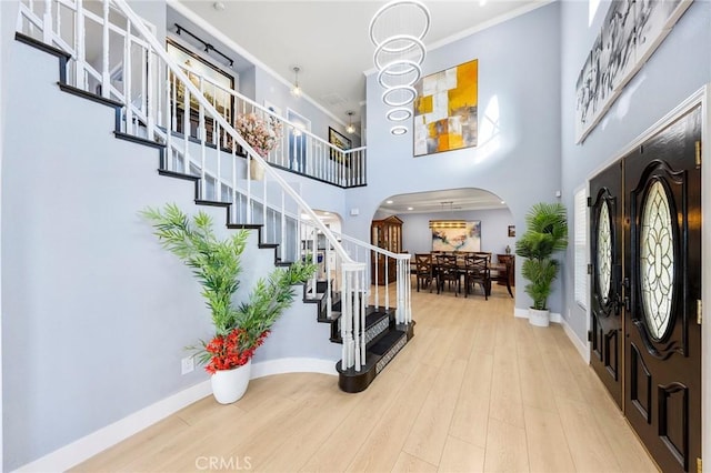 entrance foyer featuring arched walkways, a high ceiling, wood finished floors, stairway, and crown molding