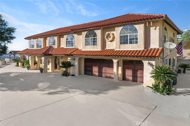 mediterranean / spanish-style home with concrete driveway, a tiled roof, an attached garage, and stucco siding