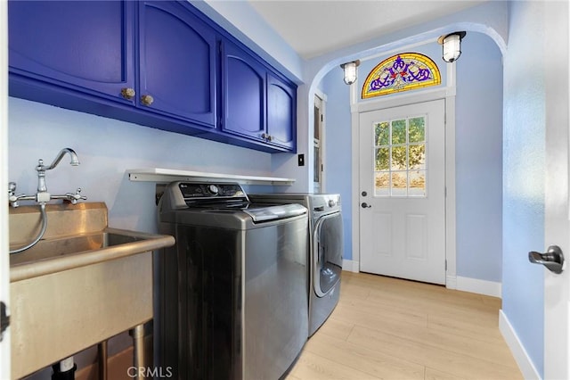 laundry room with arched walkways, washing machine and clothes dryer, cabinet space, light wood-type flooring, and baseboards