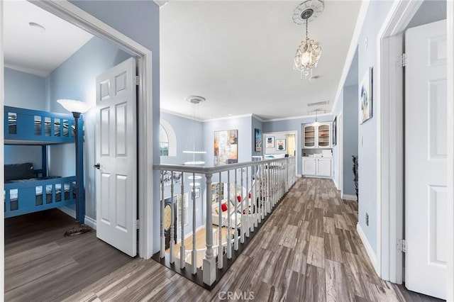 corridor featuring ornamental molding, a notable chandelier, baseboards, and wood finished floors