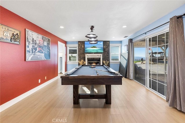 game room featuring a warm lit fireplace, pool table, a wealth of natural light, and light wood-style floors