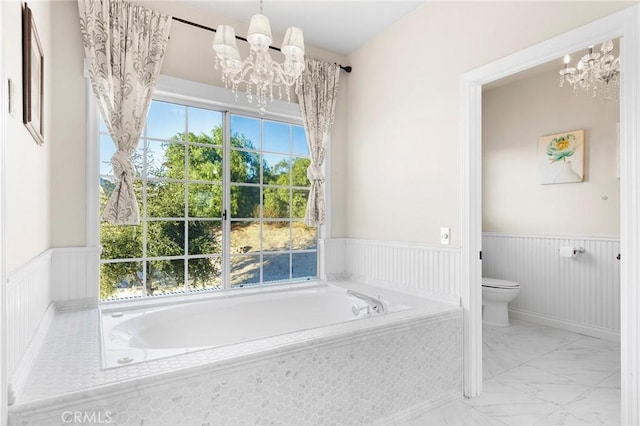 full bathroom featuring wainscoting, a notable chandelier, toilet, and a bath