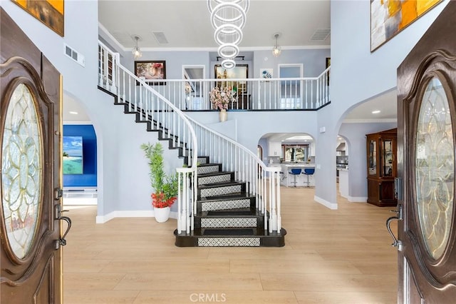 foyer entrance featuring arched walkways, visible vents, crown molding, and wood finished floors