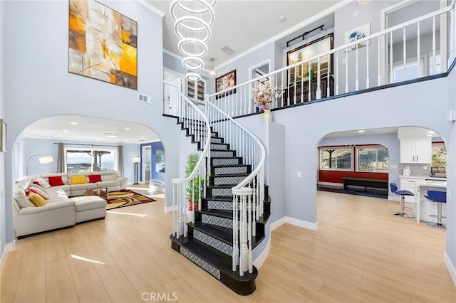 staircase featuring visible vents, arched walkways, crown molding, and wood finished floors