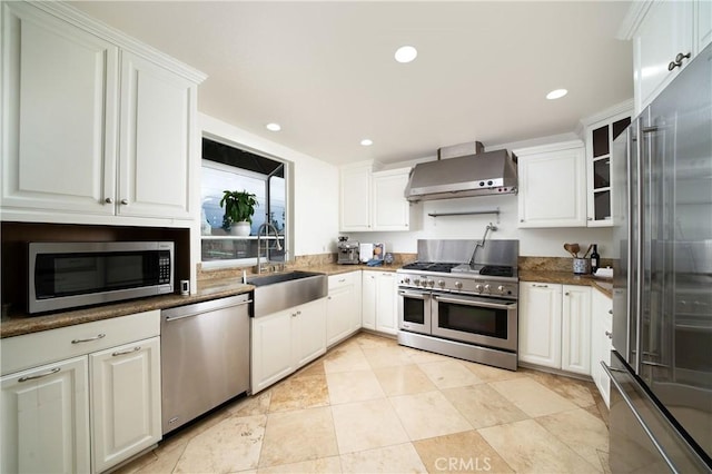 kitchen with wall chimney range hood, high quality appliances, recessed lighting, white cabinets, and a sink