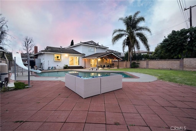 pool at dusk featuring a patio area, a fenced in pool, a water slide, and a fenced backyard