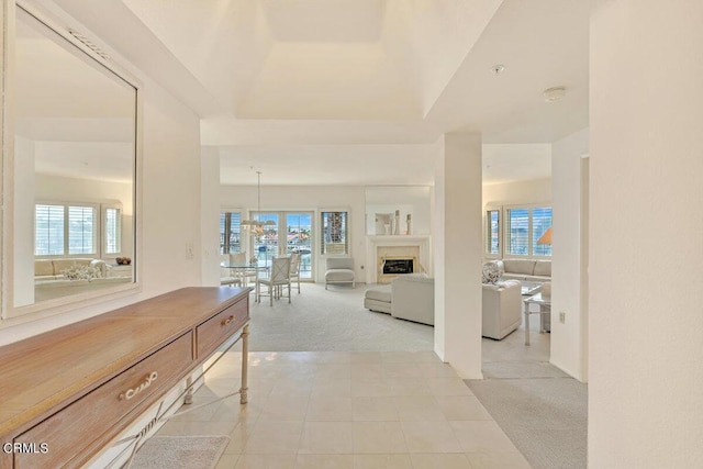 hallway with light carpet, a raised ceiling, and a wealth of natural light