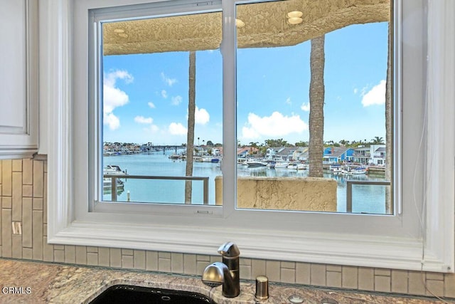 interior details with stone counters, a water view, and a sink