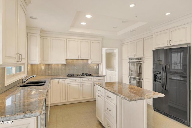 kitchen with light stone counters, double wall oven, a sink, black fridge, and a raised ceiling