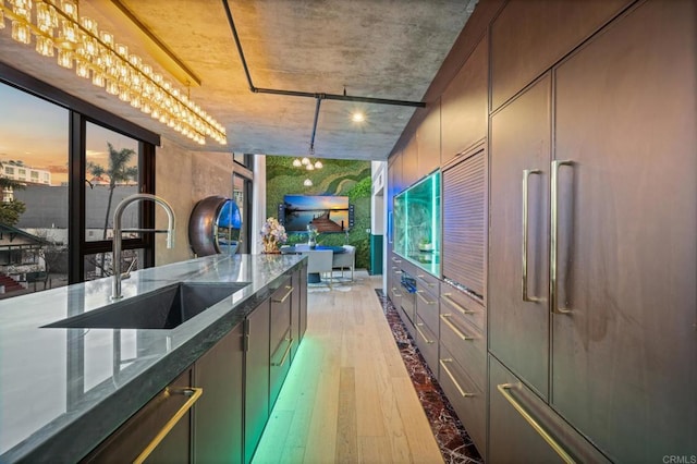 kitchen with paneled built in refrigerator, light wood finished floors, dark stone counters, and a sink