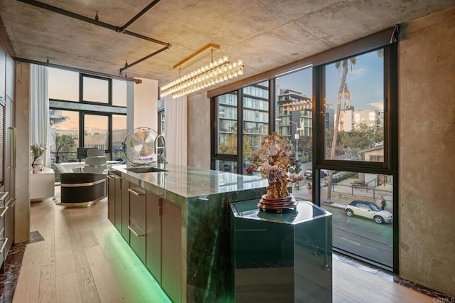 kitchen featuring light wood-type flooring, floor to ceiling windows, a sink, and an island with sink