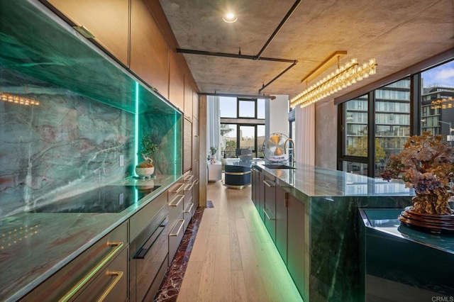 kitchen with dark stone counters, hardwood / wood-style floors, black electric stovetop, floor to ceiling windows, and a sink