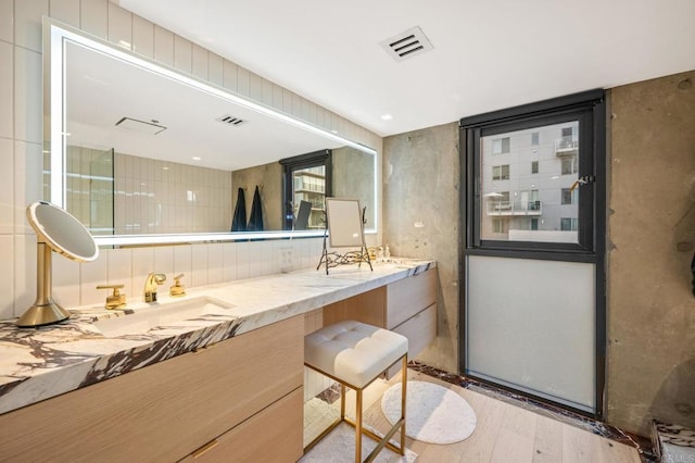 full bath featuring wood finished floors, visible vents, a sink, and double vanity